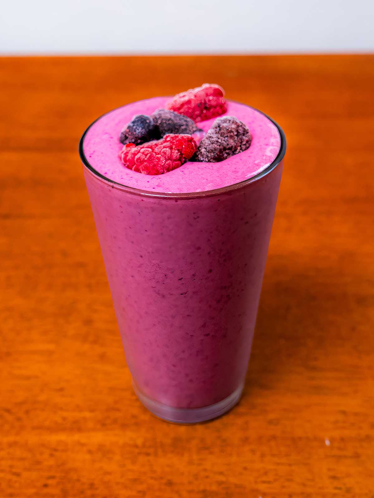 Glass of blended mixed berry protein smoothie topped with fresh mixed berries