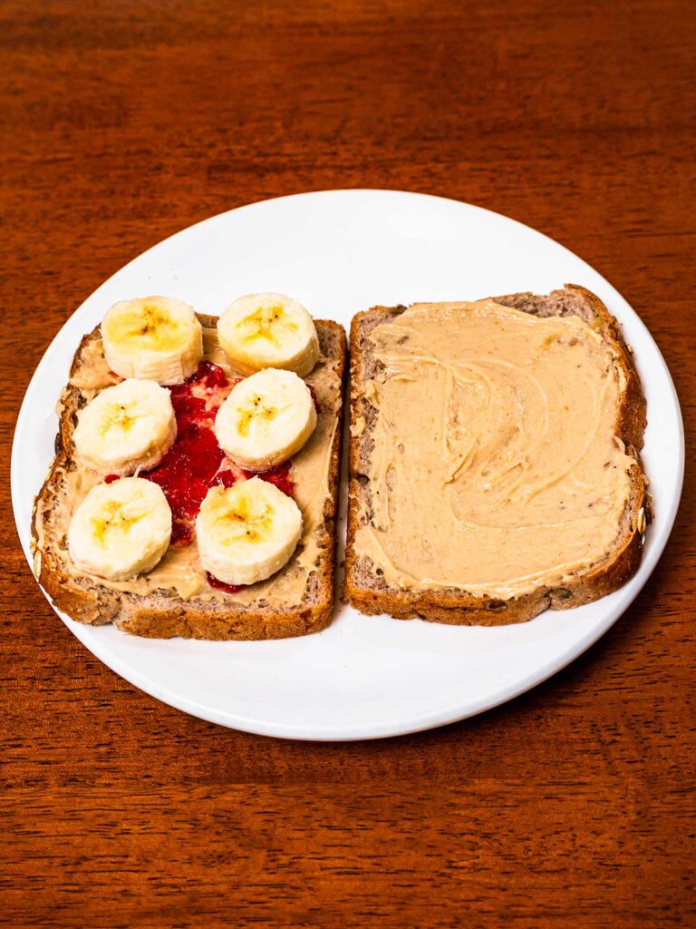 High-protein peanut butter and jelly sandwich &ndash; sliced in half on a wooden cutting board
