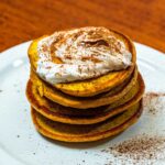 Protein pumpkin pancakes stacked on white plate &ndash; high-protein fall breakfast recipe