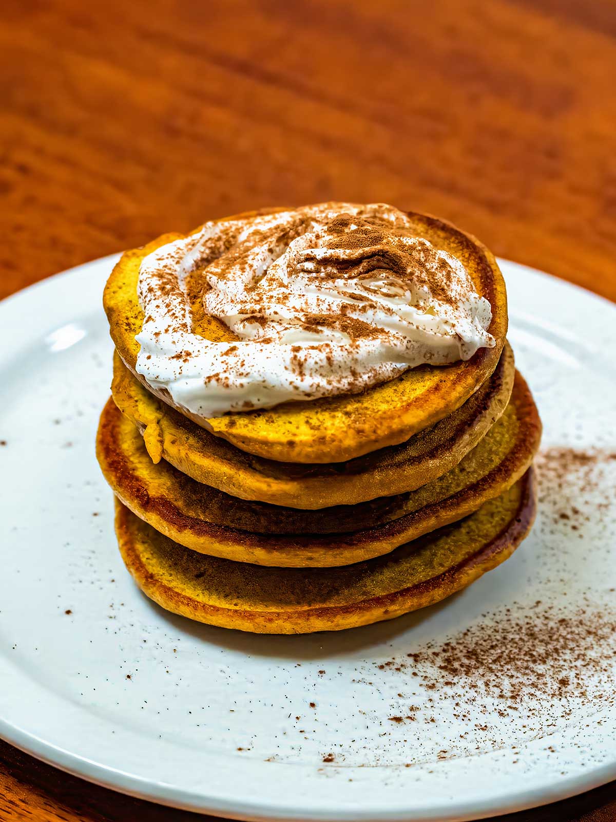 Protein pumpkin pancakes stacked on white plate &ndash; high-protein fall breakfast recipe