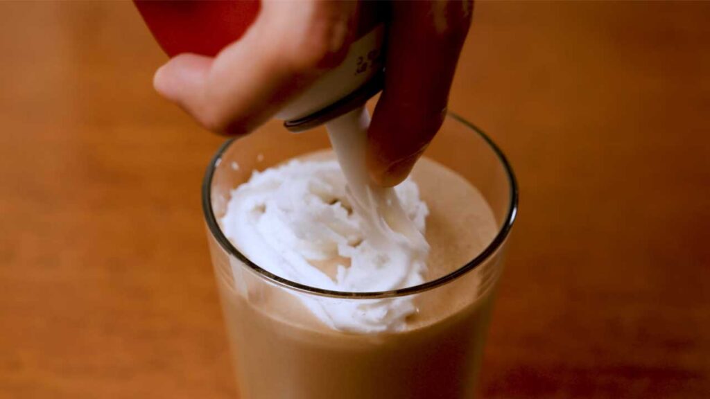 How to make tiramisu protein shake &ndash; step: pouring into glass and adding cocoa powder garnish