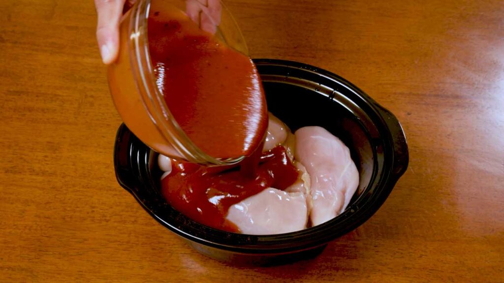 How to make slow cooker BBQ chicken &ndash; step showing chicken being seasoned and placed in slow cooker