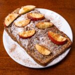 Apple cinnamon protein french toast with cinnamon apples and powdered sugar on a white plate