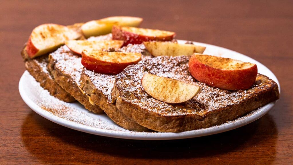 Apple cinnamon protein french toast on a white plate with apple slices and powdered sugar