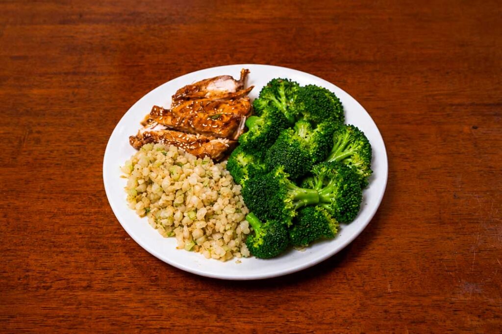 High protein meal with glazed chicken, brown rice, and broccoli on a white plate