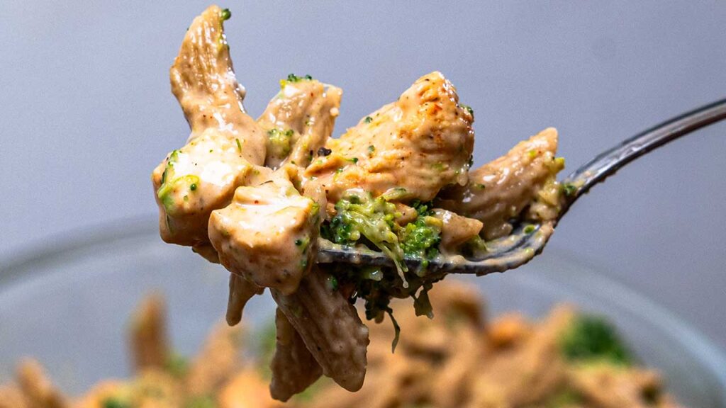 Fork lifting chicken and broccoli in cottage cheese alfredo sauce, a high-protein pasta dish