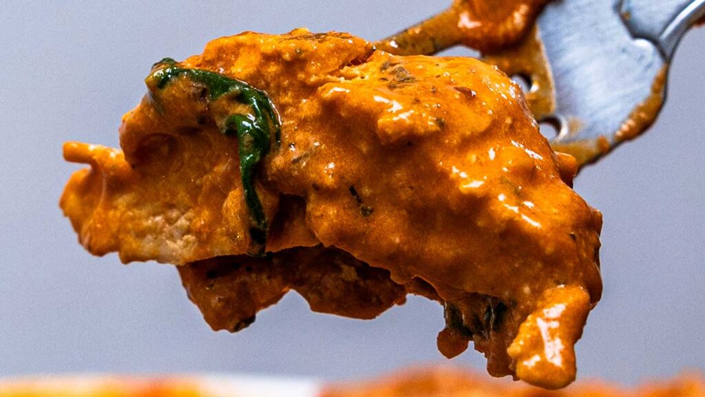 Fork lifting marry me chicken in creamy orange spinach sauce, a high-protein dish