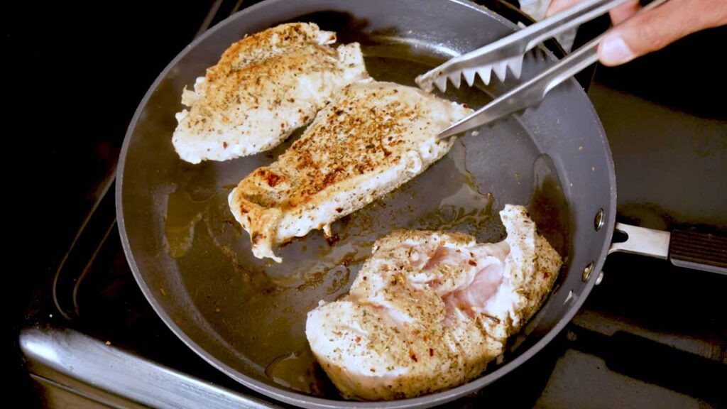 Browning seasoned chicken breasts in a skillet with tongs, a high-protein dinner step