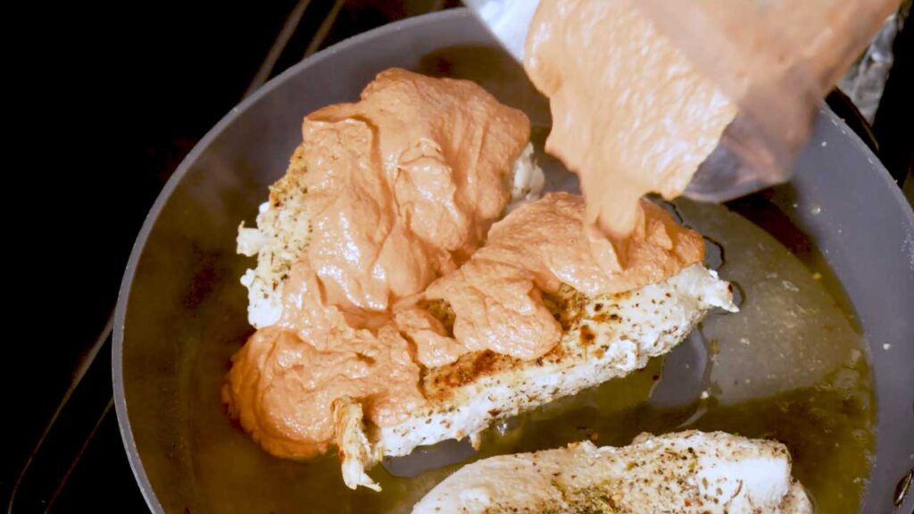 Pouring the creamy orange marry me chicken sauce over seared chicken in a skillet