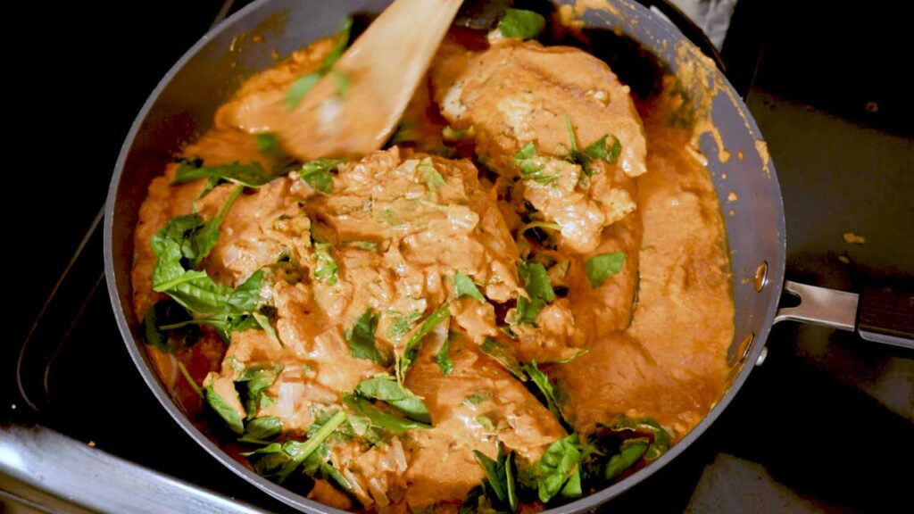 Marry me chicken simmering in a skillet with fresh spinach and orange cream sauce