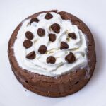 Microwave chocolate protein cheesecake topped with whipped cream and chocolate chips on a white plate