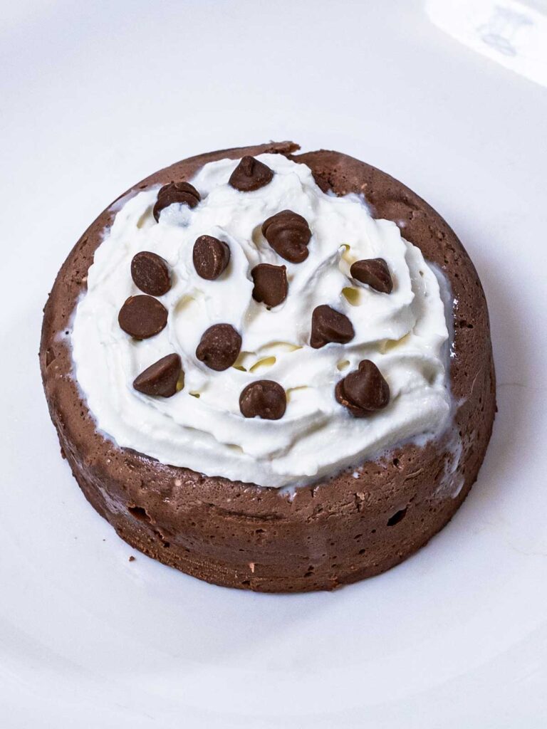 Microwave chocolate protein cheesecake topped with whipped cream and chocolate chips on a white plate