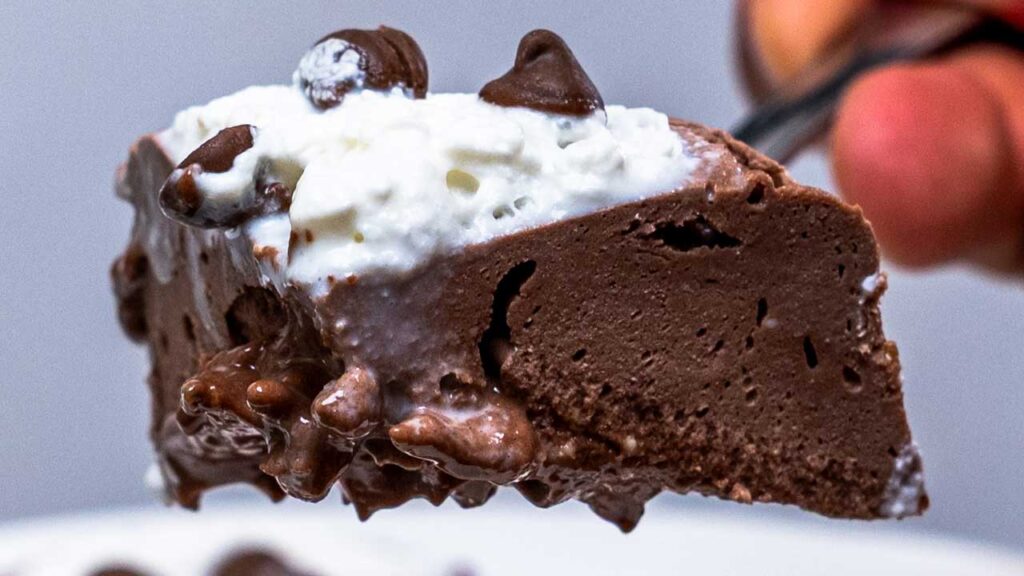 Fork lifting chocolate protein cheesecake with whipped cream and chocolate chips