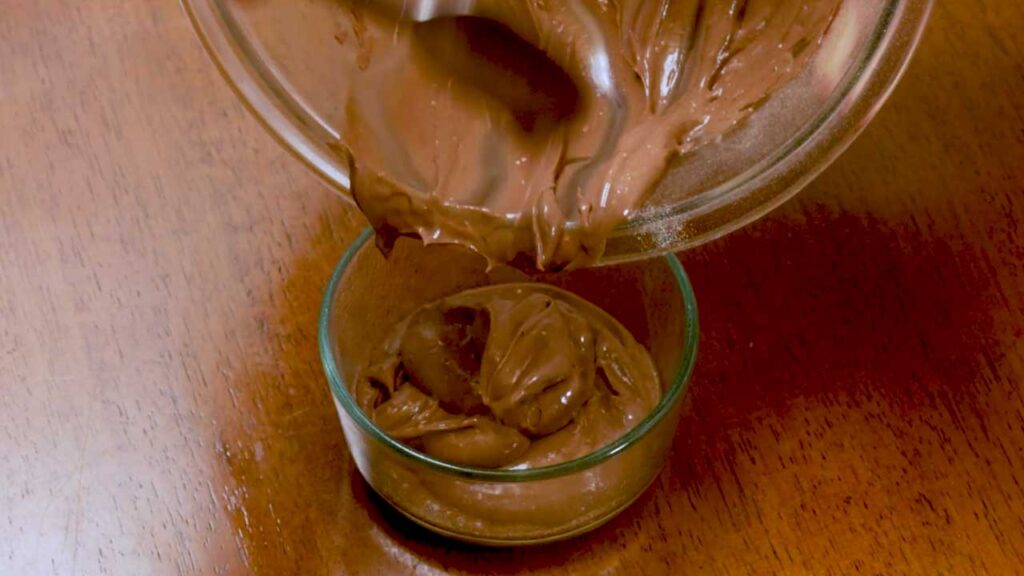 Pouring chocolate cheesecake batter into a glass ramekin for the microwave