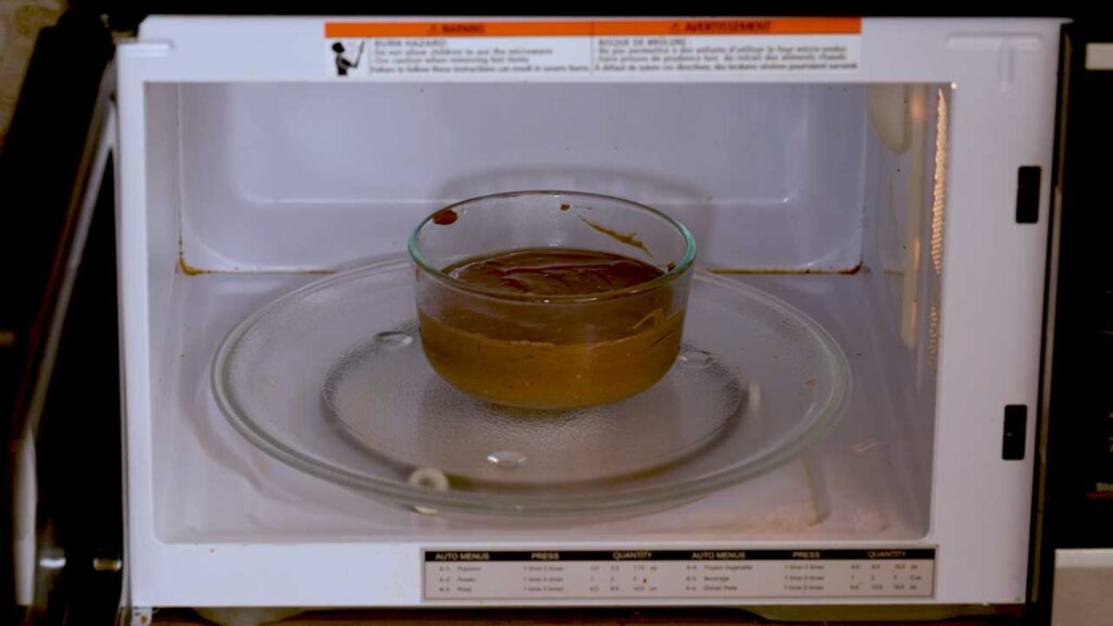 Glass ramekin of chocolate cheesecake batter inside a microwave, cooking the dessert