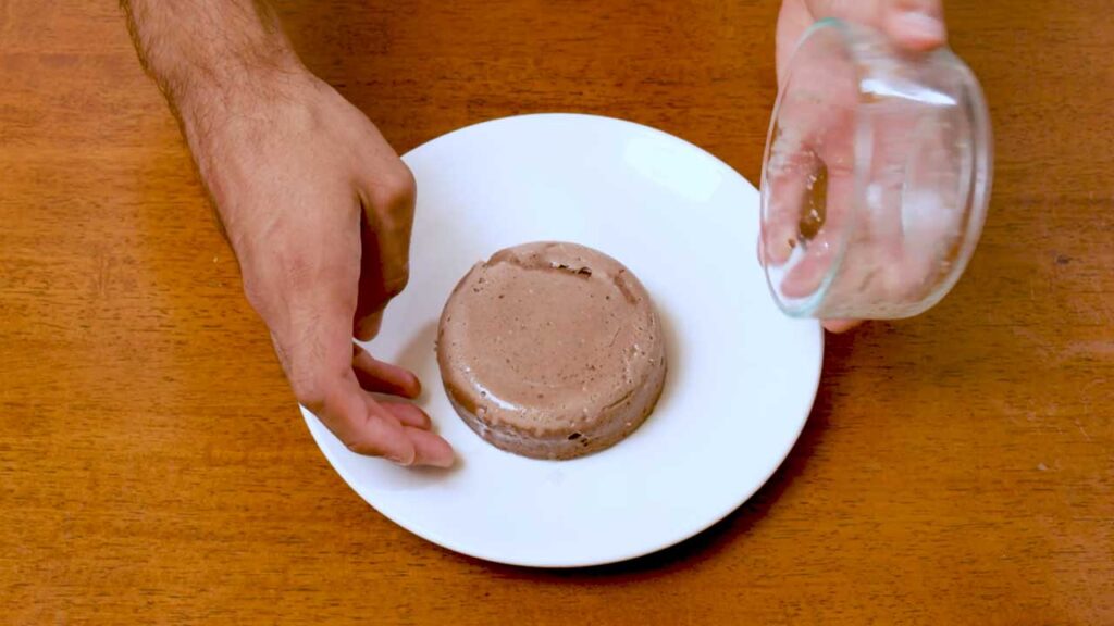 Unmolding the chocolate protein cheesecake from a ramekin onto a white plate