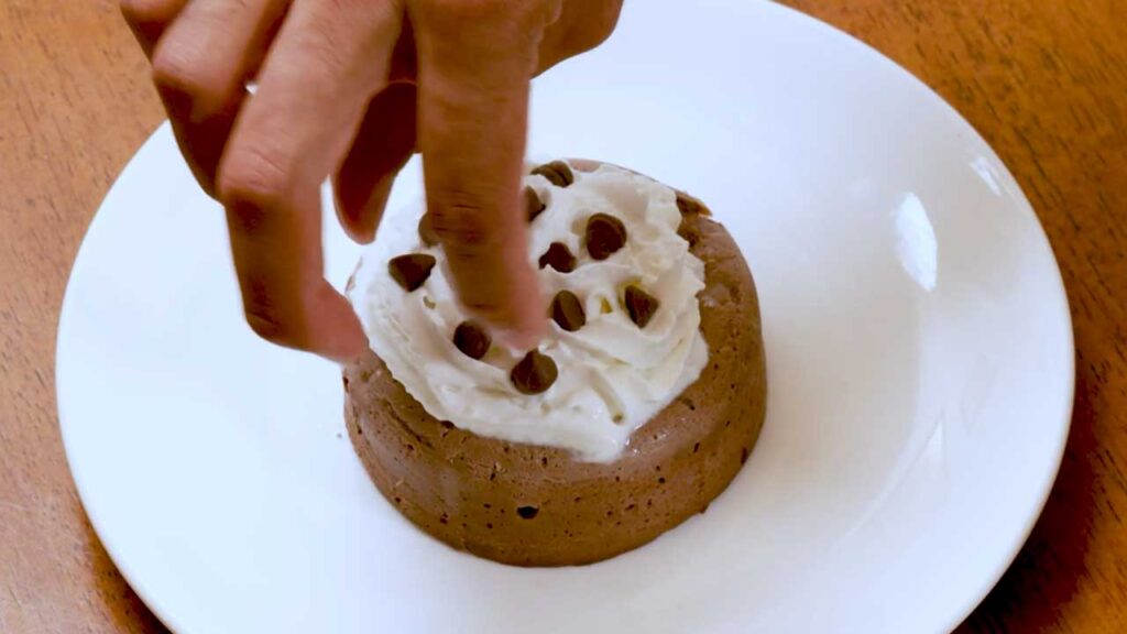 Topping the chocolate protein cheesecake with whipped cream and chocolate chips