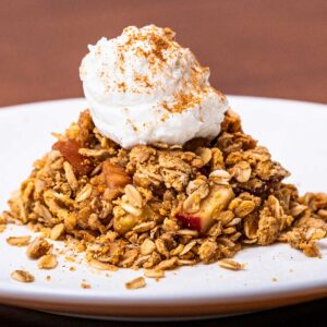Serving of high-protein apple crisp with whipped cream and a dusting of cinnamon