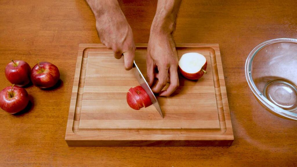 Chopping red apples into chunks on a wooden cutting board