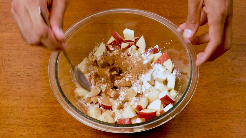 Tossing chopped apples with cinnamon and cornstarch in a glass bowl