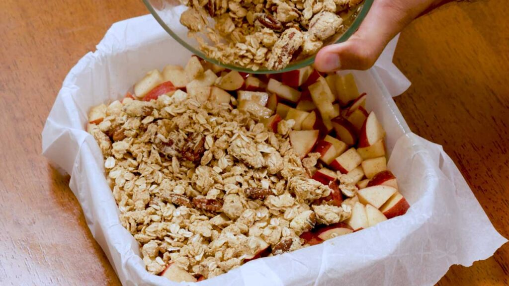 Sprinkling the oat crumble topping over the apples in the pan