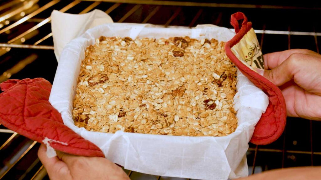 Parchment-lined pan of apple crisp being placed in the oven to bake