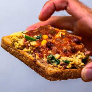 Toast topped with tex-mex cottage cheese scrambled eggs and salsa, held in hand