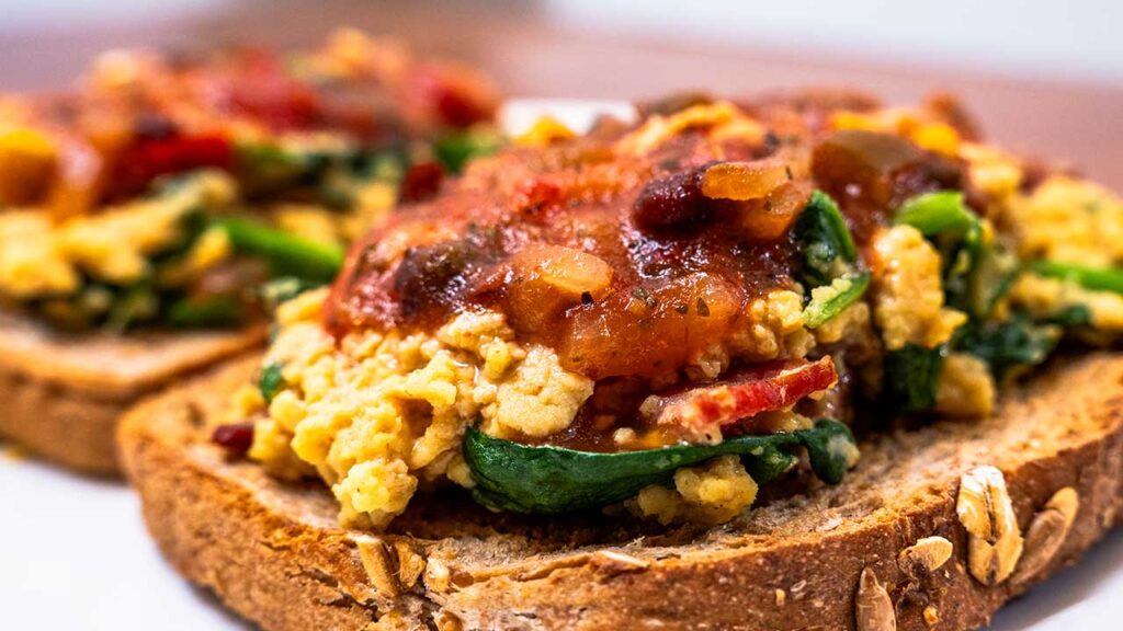 Close-up of toast with cottage cheese scrambled eggs, spinach, and salsa on top