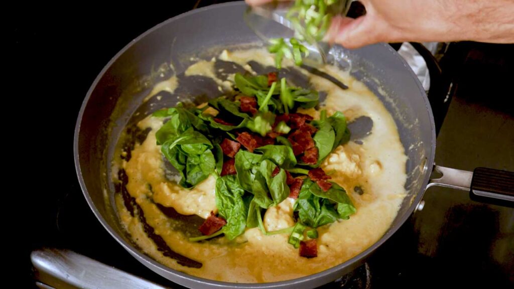 Adding spinach, jalapeno, and chorizo to the scrambling eggs in the pan