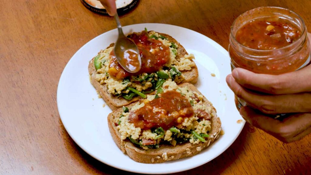 Spoonful of salsa being added to the scrambled eggs on toast