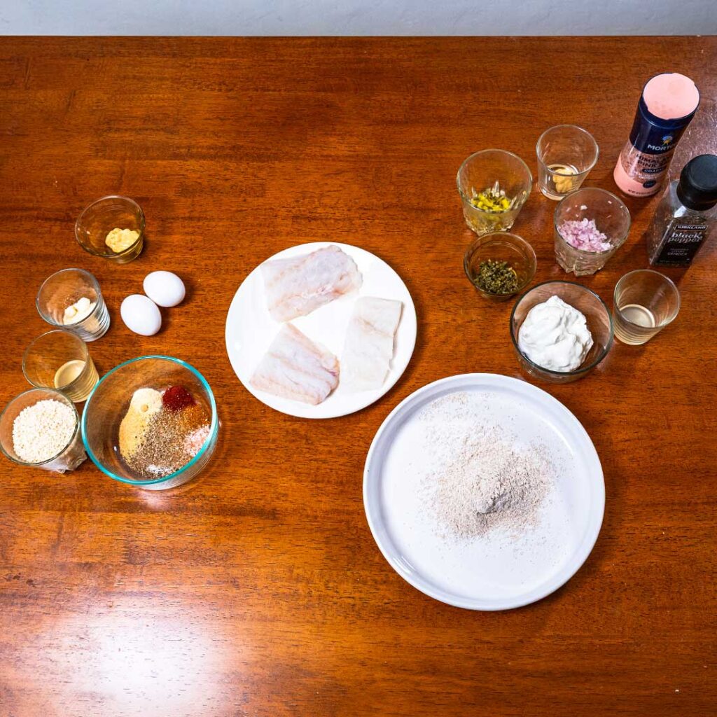 Air fryer fish sticks ingredients, raw cod, eggs, panko, and spices on a table