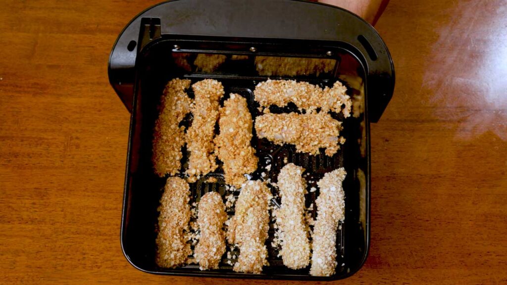 Breaded fish sticks in an air fryer basket before cooking, high protein recipe