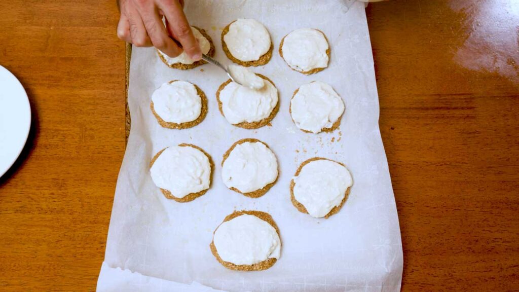 Spreading white icing over baked gingerbread protein cookies