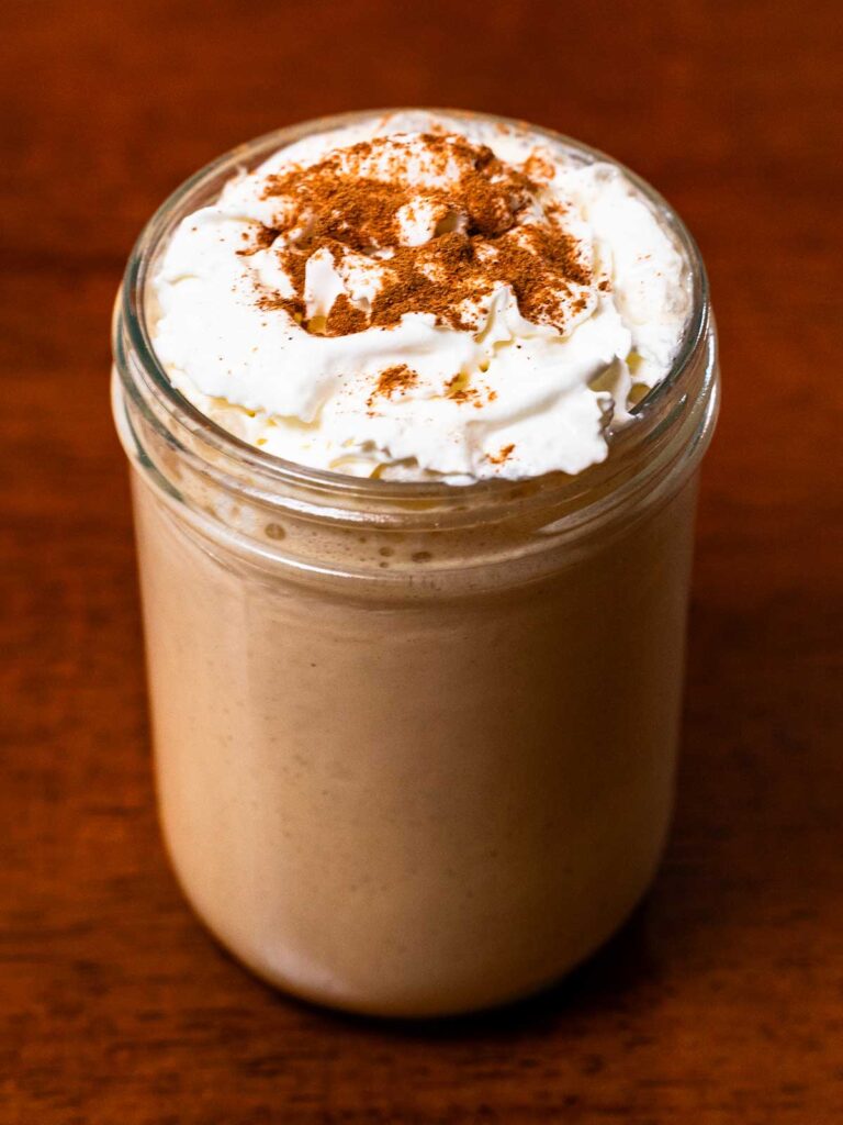 Cinnamon-spiced protein shake in a glass jar, whipped cream and gingerbread spices